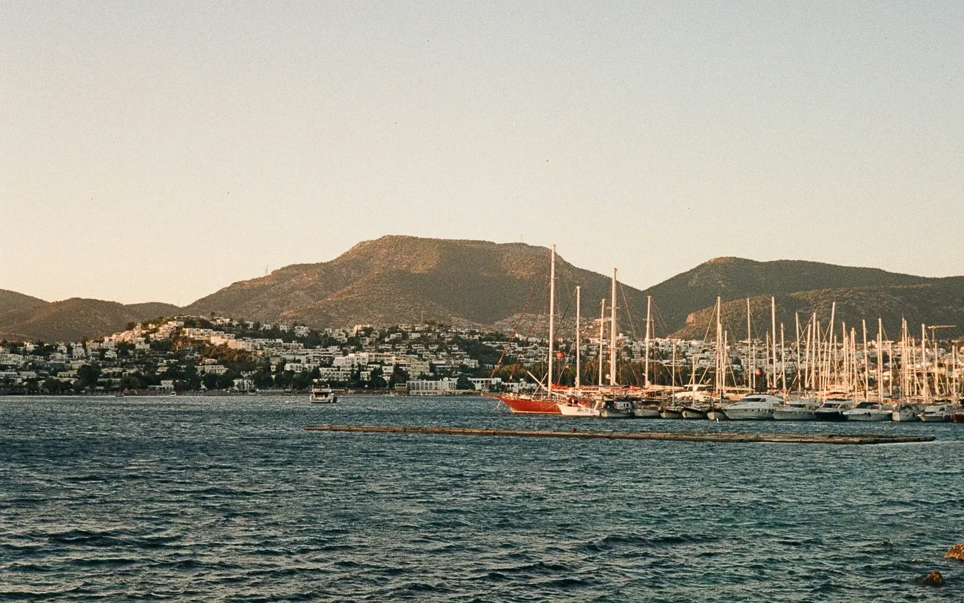 Sailing yachts moored in Bodrum's harbour below the peninsula hills at sunset